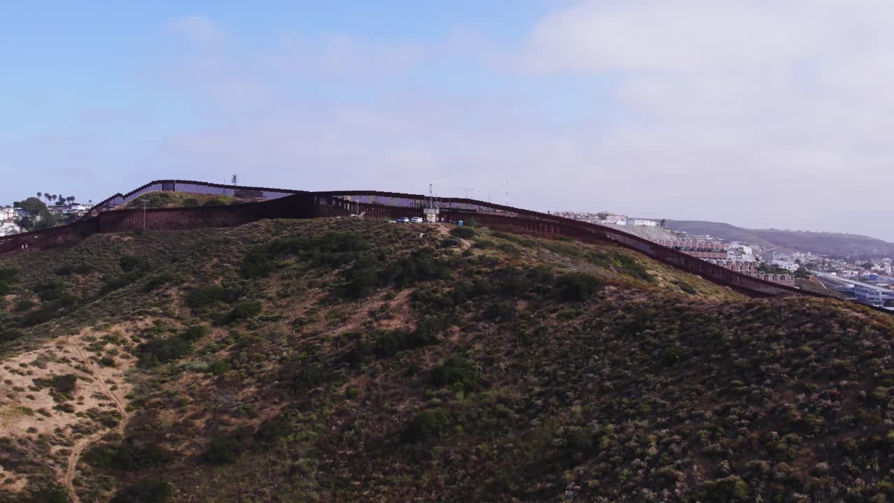 Drone footage captures a wide shot of the border wall as it snakes through rugged terrain and separates Tijuana from southern California.