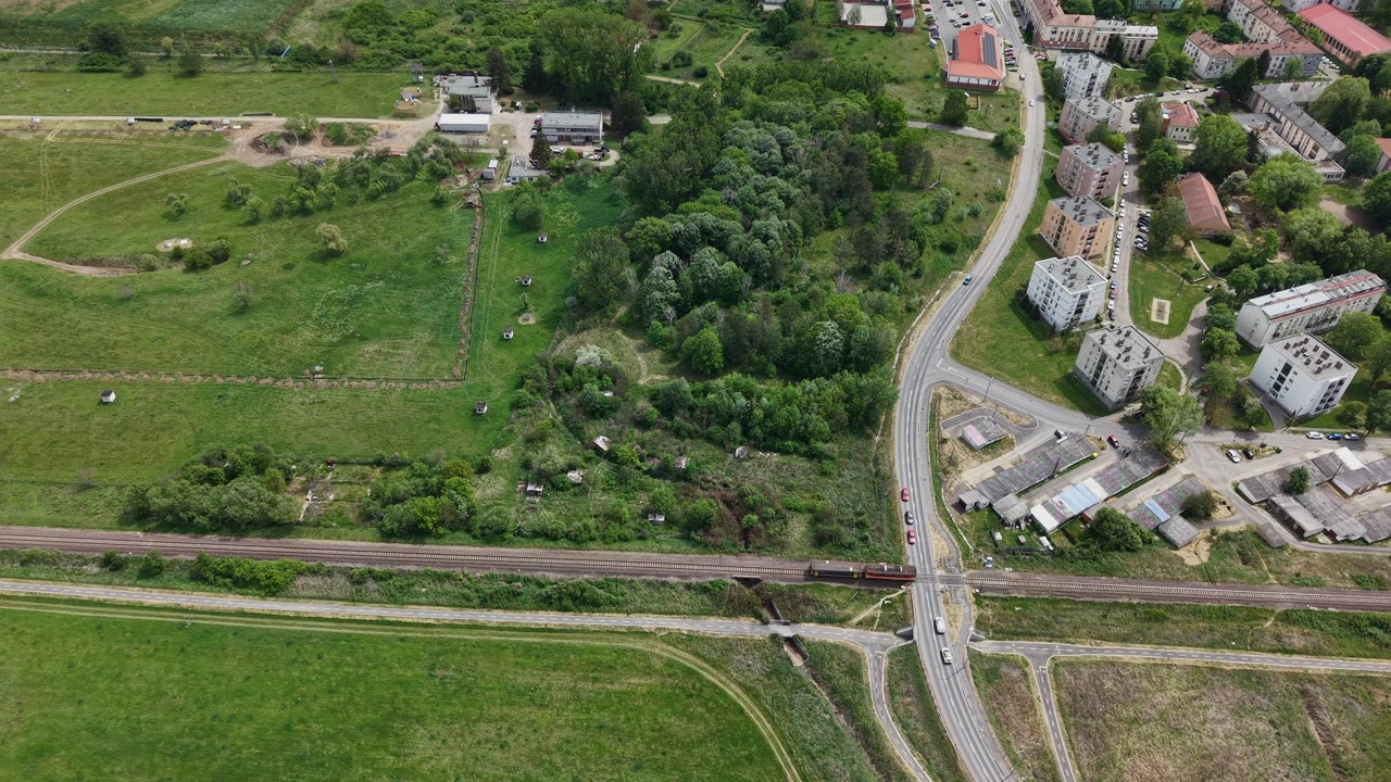 Una prospettiva aerea cattura un treno che attraversa un paesaggio rurale accanto a un piccolo quartiere di condomini residenziali.