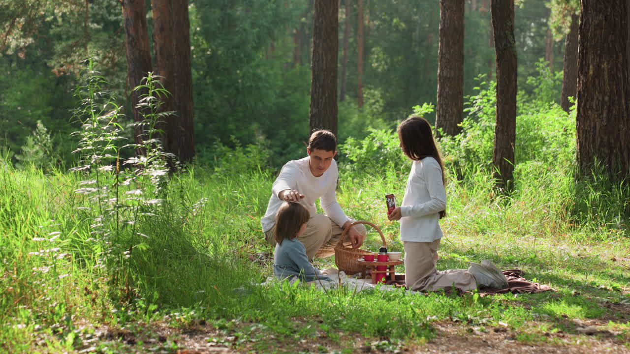 Siblings sitting together on picnic mat surrounded by sunlight and lush forest greenery, enjoying calm outdoor afternoon, sharing snacks and smiles, reflecting warmth, and togetherness