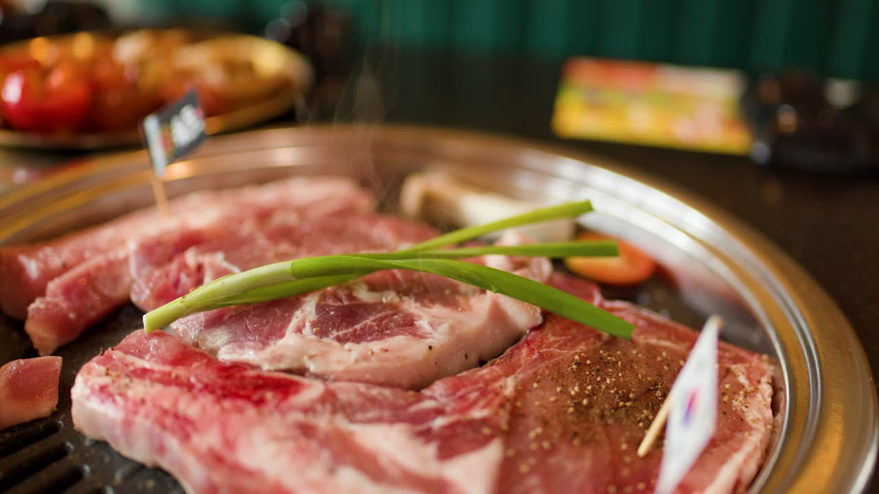 Raw beef and lamb grilling on metal pan with steam, warm lighting, shallow focus
