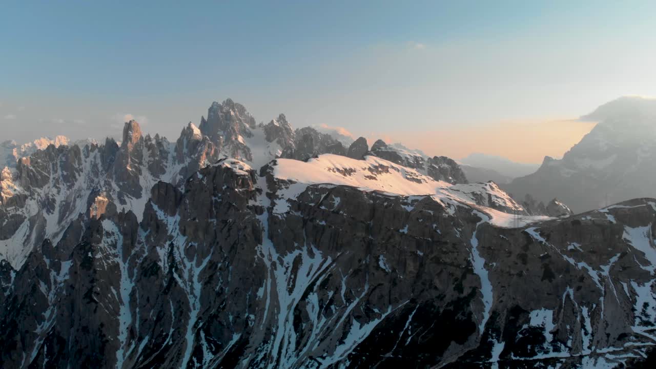Aerial 4K drone shot panning across snow-capped Dolomites at sunset. Stunning winter mountain landscape with golden hour light and dramatic alpine scenery.