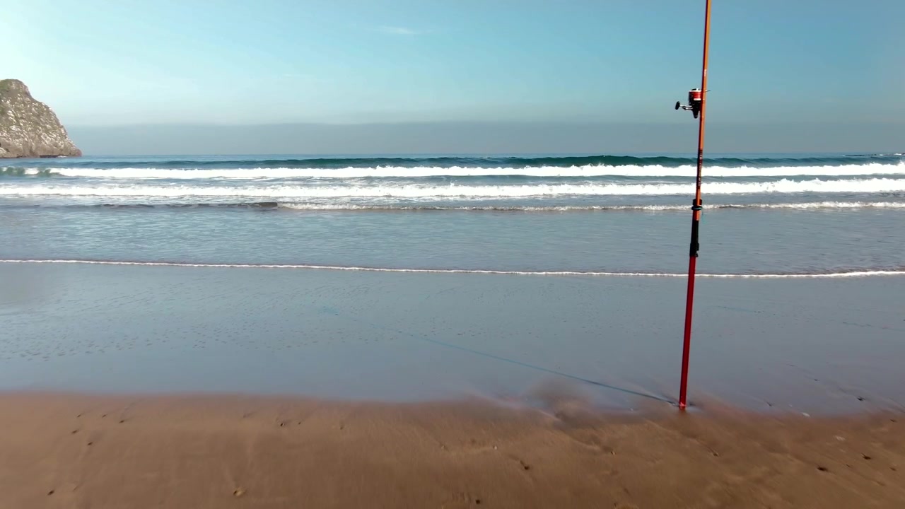 Ensom fiskestang står på sandstrand i kystområde i Spanien, luftfoto, set fremad