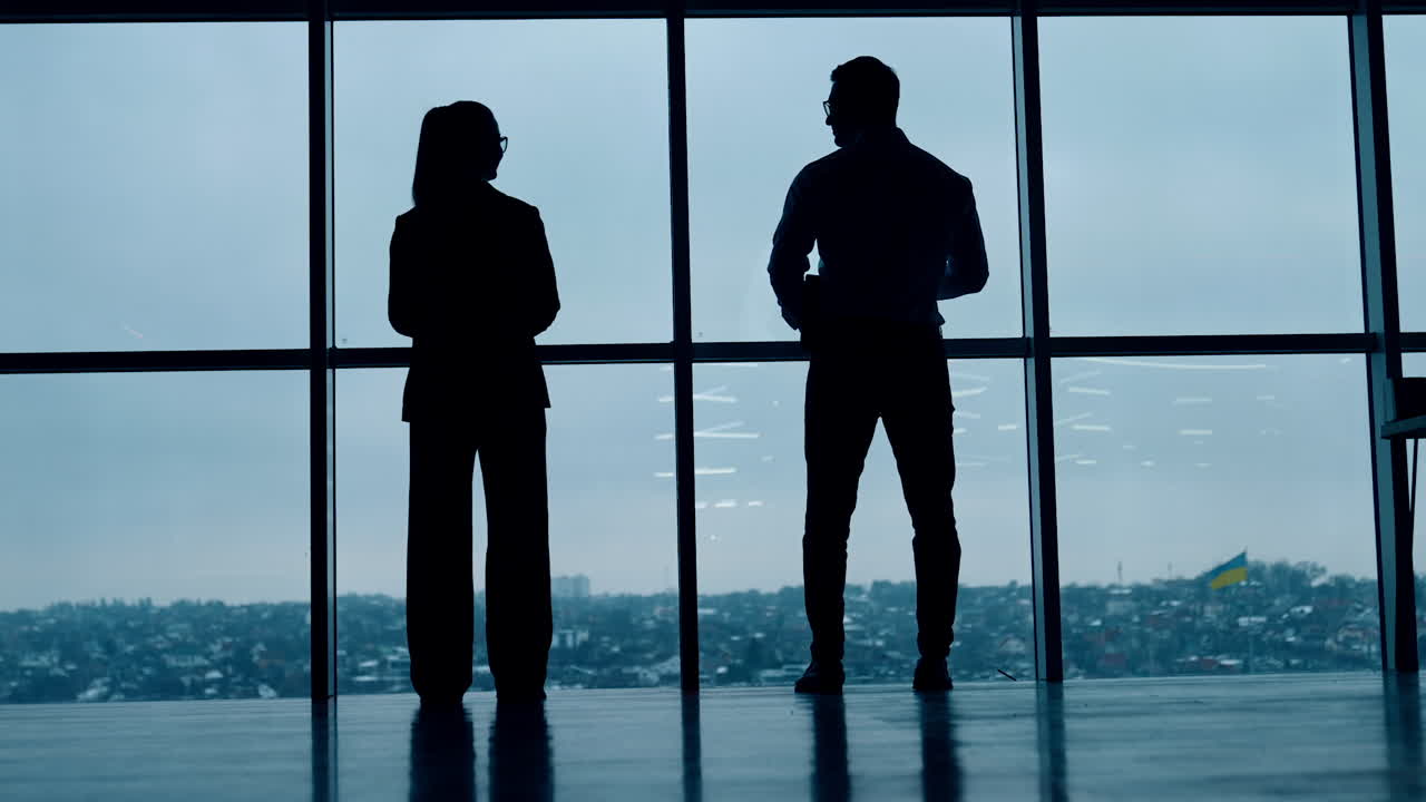 Two full-length silhouettes standing at the window. Male and female stand back to the camera looking at panoramic window.