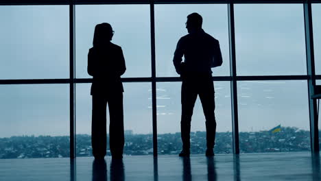 two full-length silhouettes standing at the window. male and female stand back to the camera looking at panoramic window.