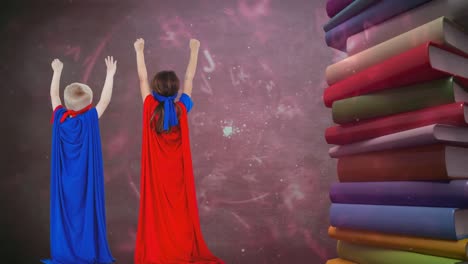 Animation-of-letters-moving-over-boy-and-girl-in-superhero-capes-with-stack-of-books