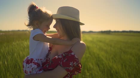 Eine-Junge-Mutter-Mit-Hut-In-Nahaufnahme-Hält-Ihre-Kleine-Tochter-Im-Arm-Und-Steht-Auf-Dem-Feld.-Der-Wind-Weht,-Die-Haare-Flattern