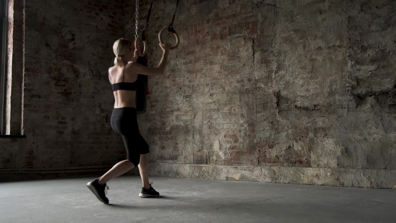 chica deportiva haciendo saltos en anillos deportivos. joven mujer en forma haciendo estiramientos en anillos de gimnasia. joven atleta femenina musculosa haciendo ejercicios con anillos en el gimnasio. joven chica en forma haciendo pull-ups en anillos gimnásticos