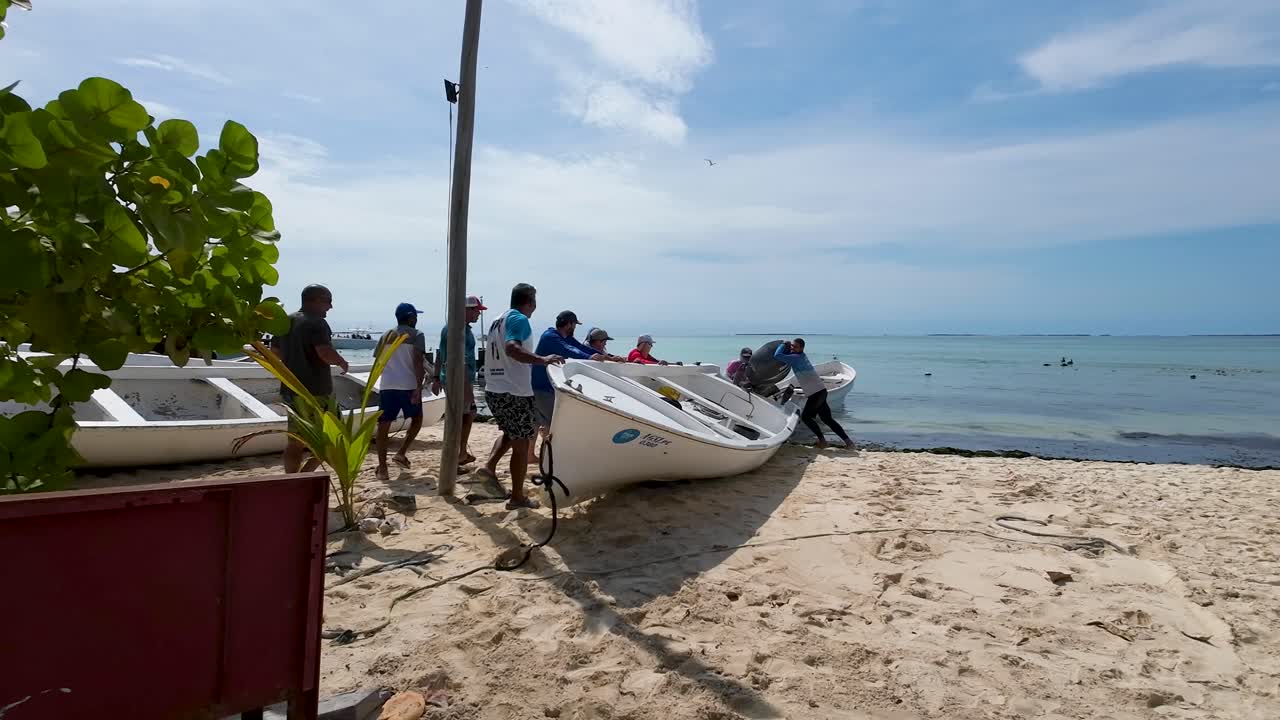 Group of men together lift fishing boat to beach it on shore beach, Los Roques Venezuela