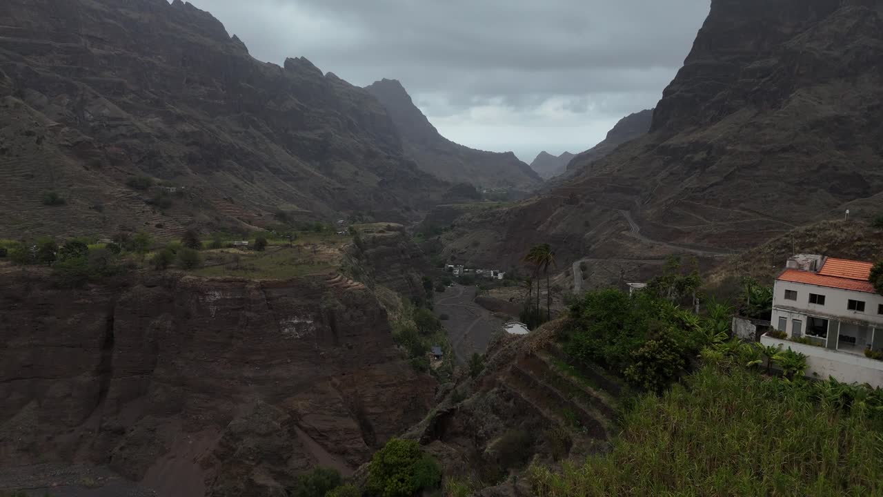 Vista aerea cinematografica di una casa solitaria circondata da una vegetazione lussureggiante e imponenti pareti montuose in una profonda valle di Santo Antão, Capo Verde. Natura selvaggia di un'isola tropicale remota e sentiero escursionistico