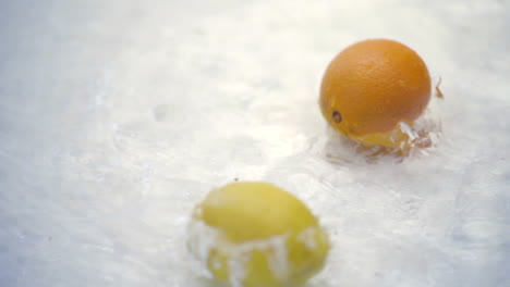 slomo of citrus falling into water on white backdrop