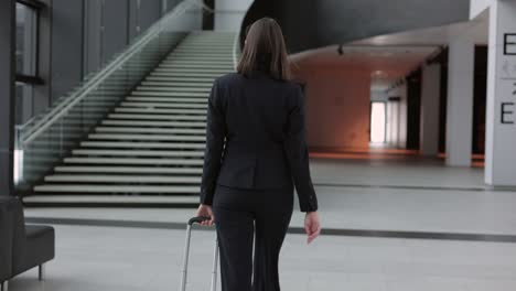 business woman in a business suit with a suitcase walks through the airport or business center and talks on the phone. a european confident woman