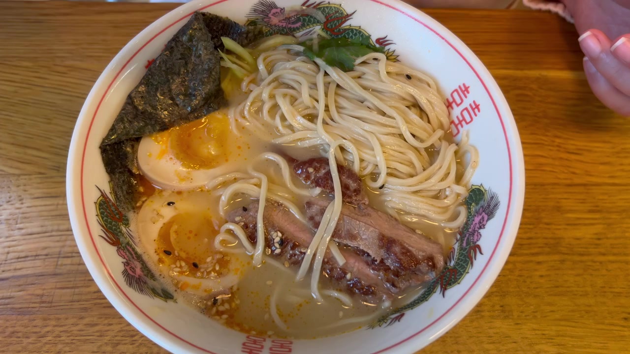 Primo piano di un cucchiaio giapponese che raccoglie ramen tonkotsu fumante con ricco brodo di maiale, fette di maiale chashu, uovo semi-sodo, alga nori e cipollotti verdi.