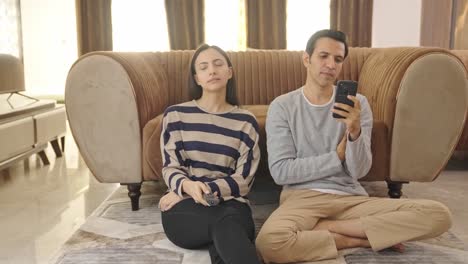 la esposa india está viendo televisión y el marido está ocupado en el teléfono.