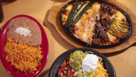 overhead shot of table filled with plates of fajitas, mexican rice, refried beans, sour cream, guacamole, hd