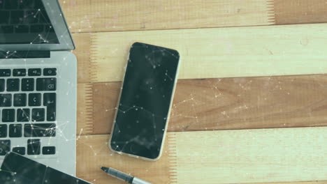 animación de una red de iconos digitales contra una tableta digital, una computadora portátil y un teléfono inteligente en una mesa de madera