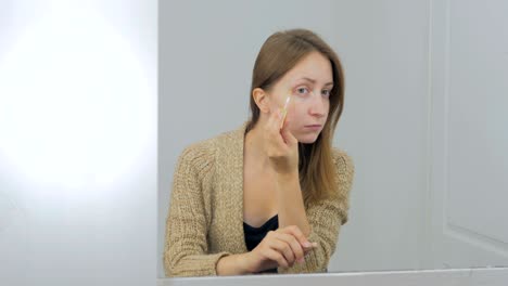 una joven hermosa se aplica un corrector, una crema de fundación y un maquillaje.