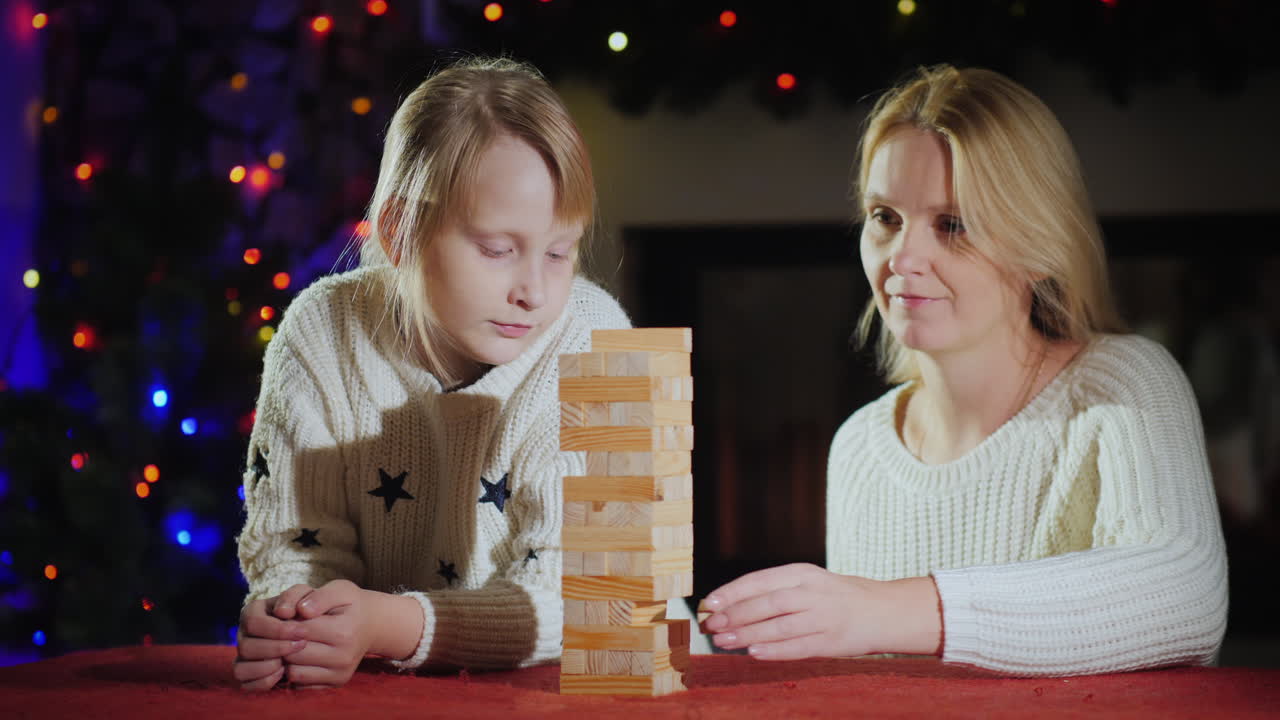 chica con mamá juega un juego de mesa en el fondo de luces borrosas de guirnaldas festivas