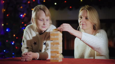 girl with mom play a board game on the background of blurry lights of festive garlands