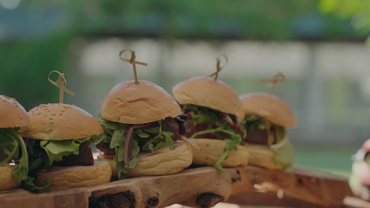 Close up of artisan mini burgers with lettuce and beef patties arranged on a wooden board for catering or event service