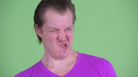 studio shot of young man looking disgusted against green background