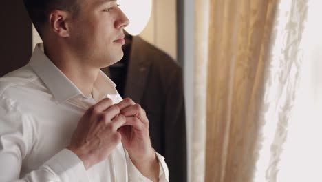 stylish man in jacket fastens buttons, buttoning white shirt preparing to go out near window