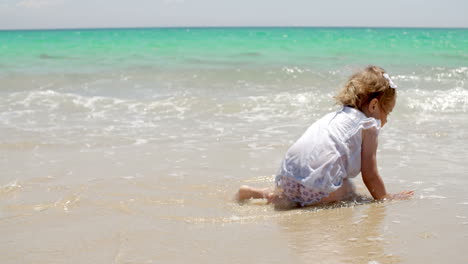 Kleines-Mädchen-Sitzt-An-Einem-Strand-In-Der-Nähe-Des-Wassers