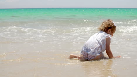 little girl sitting on a beach close to the water