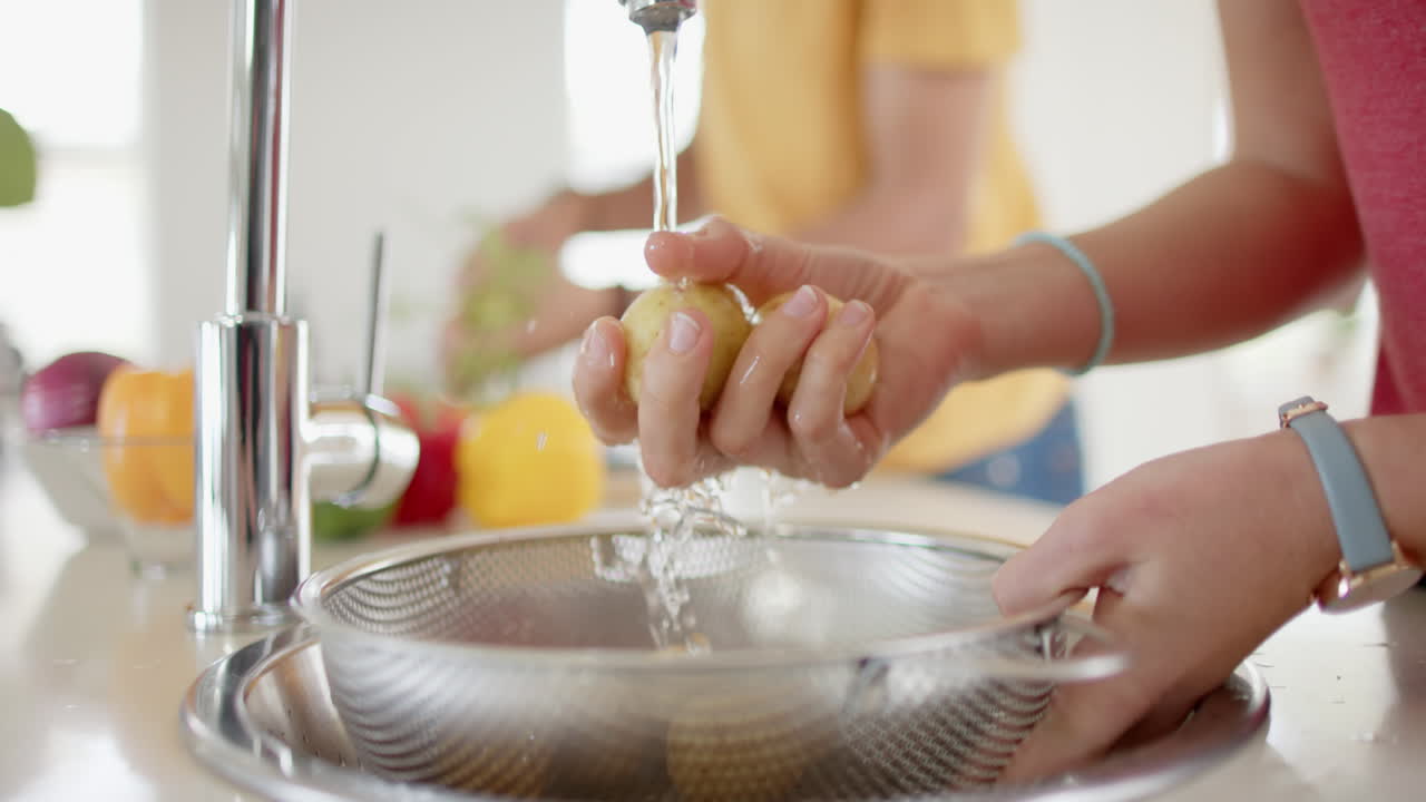 Pareja diversa preparando y lavando verduras frescas en la cocina, cámara lenta