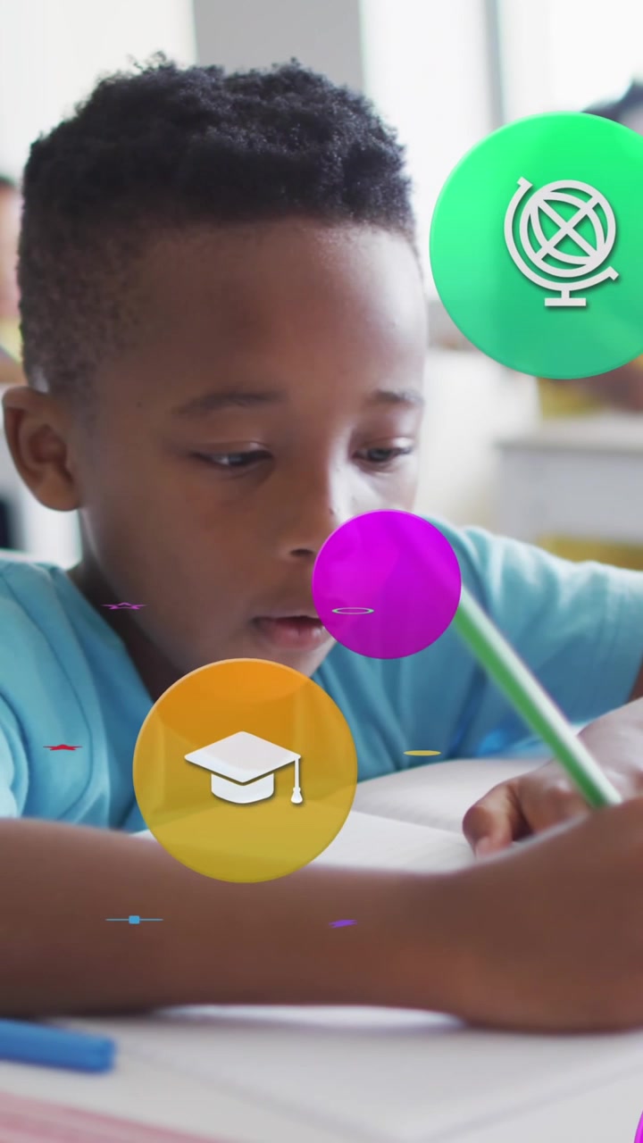 Animation of school icons over busy african american schoolboy working at desk in class