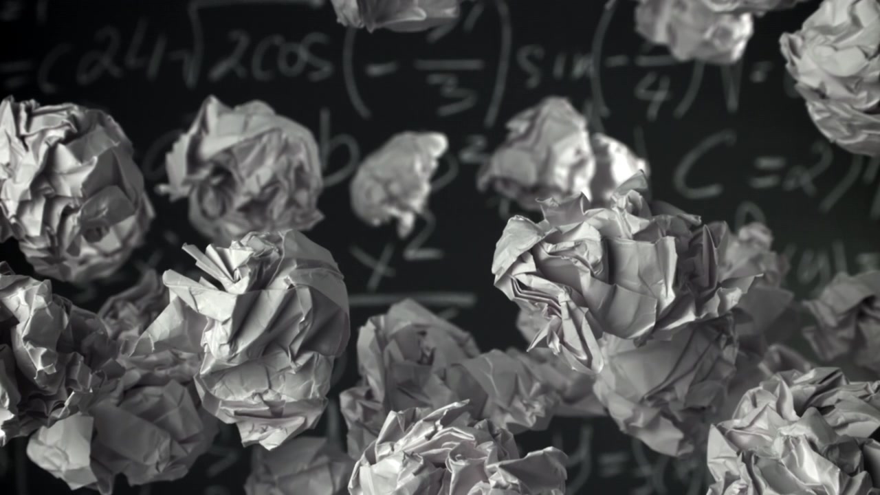 Boules de papier froissées s'élevant devant un tableau noir avec des équations mathématiques.