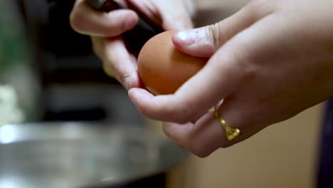a hand cracks a brown egg using a knife over a bowl in a kitchen. slow motion