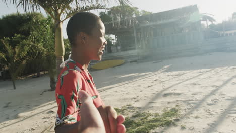 feliz mujer biracial en vestido rojo bailando y riendo en la playa soleada, cámara lenta