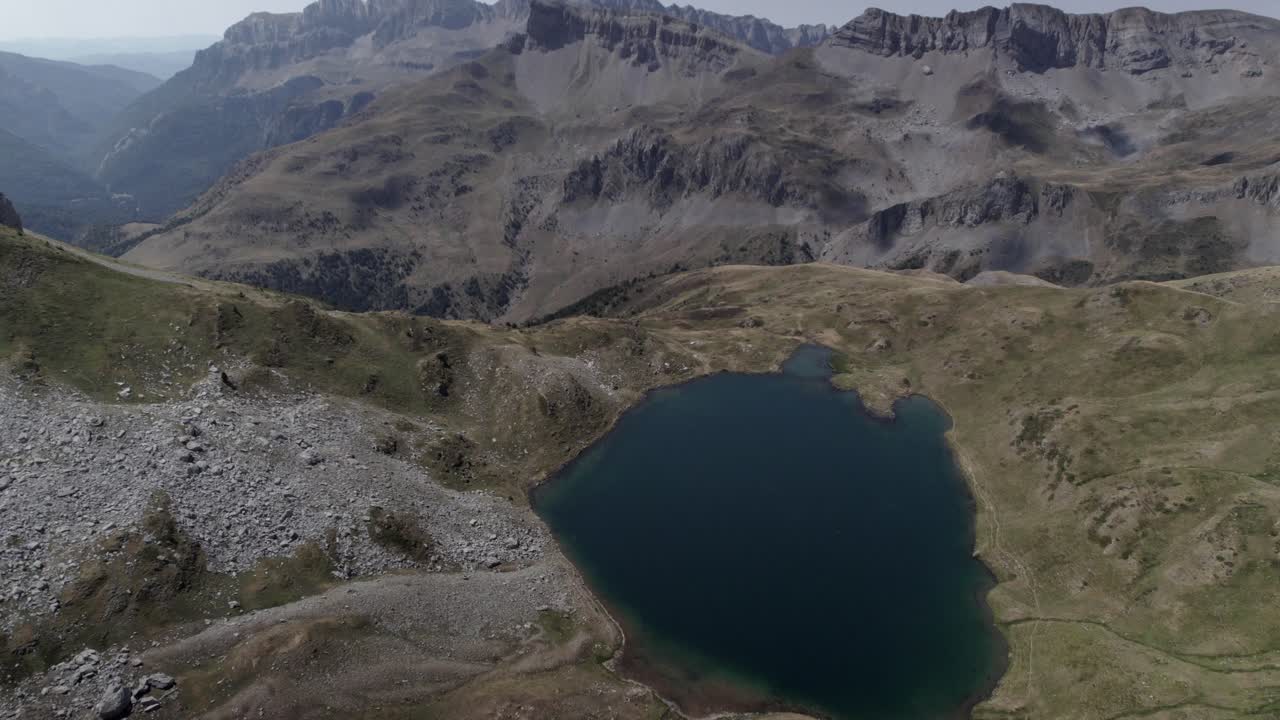 4K bird’s-eye drone shot over Ibón de Acherito in the Western Valleys Natural Park, Aragonese Pyrenees, Spain. A stunning aerial view of the alpine lake surrounded by rugged mountains.