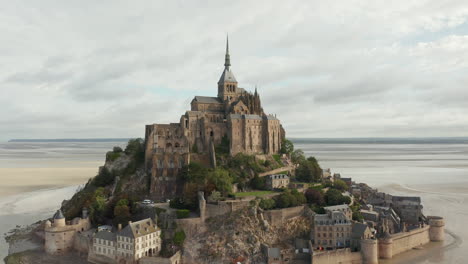 Wide-View-of-Le-Mont-Saint-Michel-Castle-in-the-Ocean-in-France,-Aerial,-Cloudy