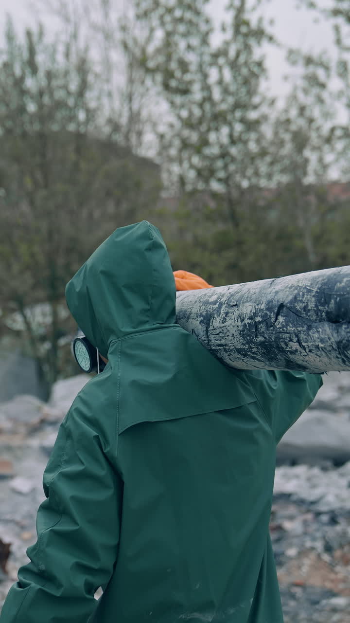 Man in safety suit walking in dangerous zone. Human in protective uniform and respirator is carrying pipe in the abandoned place with polluted air. Rear view. Vertical video