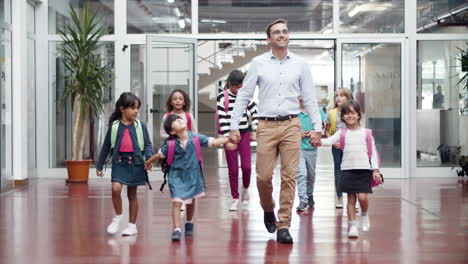 Smiling-male-teacher-with-group-of-children-walking-in-school-corridor-and-going-to-class