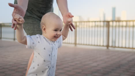 Madre-Joven-Con-Un-Niño-Y-Primeros-Pasos.-Madre-Joven-Con-Un-Niño-En-El-Aprendizaje-Al-Aire-Libre-Para-Dar-Los-Primeros-Pasos-Cerca-De-La-Ciudad-Urbana