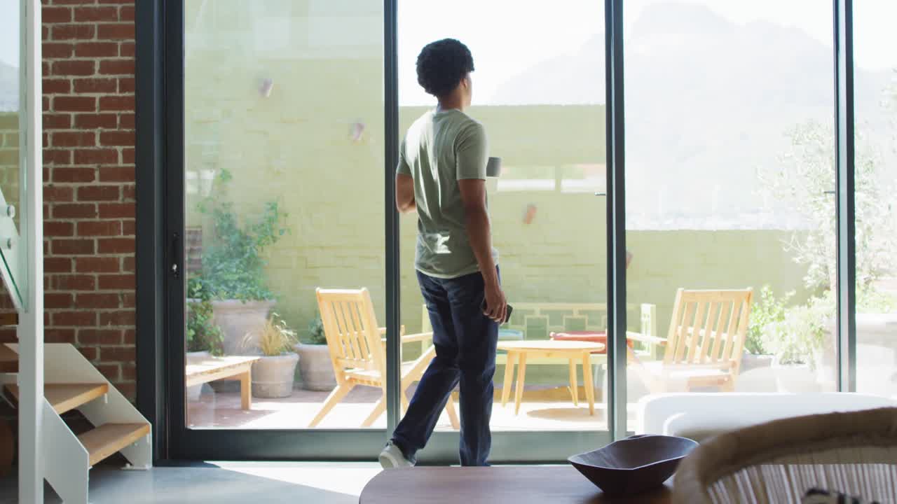 아프리카계 미국인 남자가 집에서 스마트폰을 사용하고 커피를 마시고 있습니다.