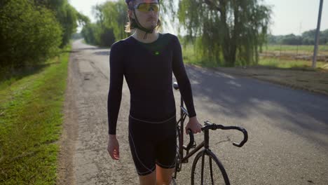 male cyclist walks down the road and rolls his bike beside him