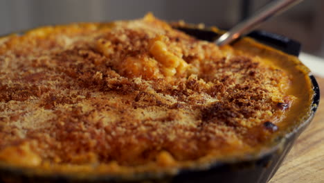 Tenedor-Cavar-En-Una-Sartén-De-Hierro-Fundido-Llena-De-Macarrones-Con-Queso,-Un-Clásico-Plato-Americano,-Horneado-En-El-Horno-Con-Migas-De-Pan-Crujientes-En-La-Parte-Superior