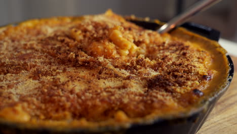 tenedor cavar en una sartén de hierro fundido llena de macarrones con queso, un clásico plato americano, horneado en el horno con migas de pan crujientes en la parte superior