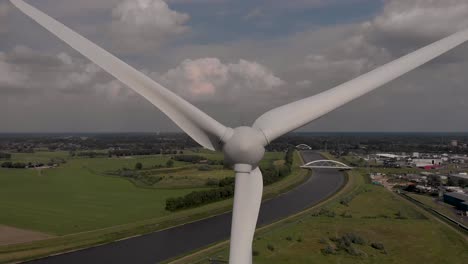 rotating blades aerial closeup approach of wind turbine with dutch waterway infrastructure twentekanaal in flat landscape
