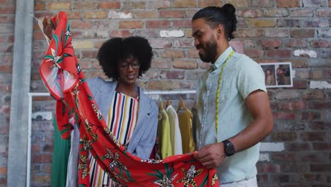 diverse male and female fashion designers in discussion at work looking at dress