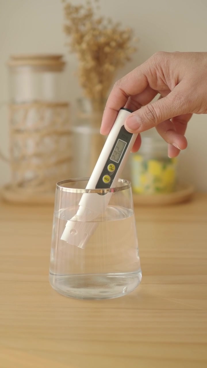 Mano che misura la qualità dell'acqua con un misuratore TDS in un bicchiere