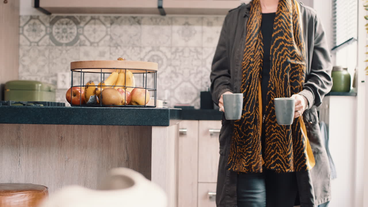 Woman walking from the kitchen with 2 cups of coffee in her hand towards the living room