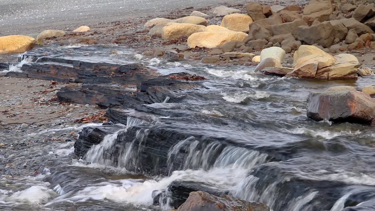 Água fluindo de um riacho largo sobre rochas, criando uma pequena cachoeira na praia na Península de Kenai, Alasca
