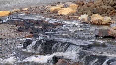 water flowing from a wide stream flowing over rocks creating a small waterfall on beach in kenai peninsula of alaska