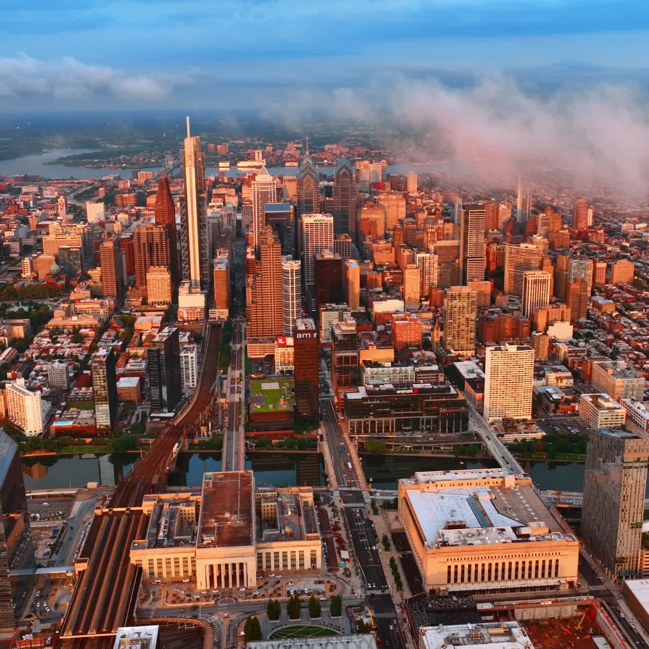 Setting sun lighting beautiful buildings of Philadelphia downtown. White clouds floating above the skyscrapers. Top view
