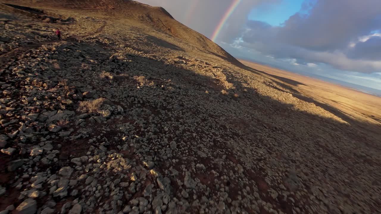 Hiker on path over volcanic landscape in Fuerteventura. Sunrise scene with clouds. Stony and rocky landscape of Calderón Hondo Volcano.