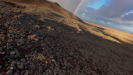 hiker on path over volcanic landscape in fuerteventura. sunrise scene with clouds. stony and rocky landscape of calderón hondo volcano.